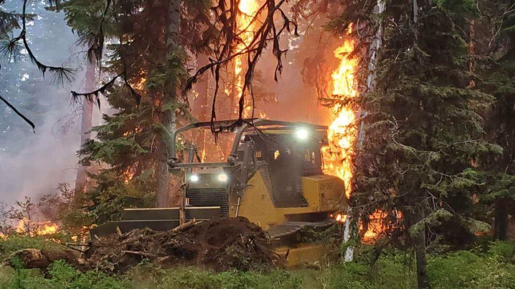 Dozer creates fire line with burning trees in background